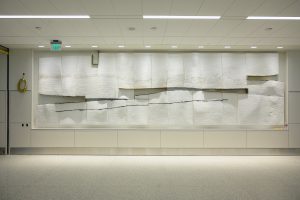 A view of Near Distance, a public art installation in the NEW SLC airport made of white plaster panels with balck charcoal streaks. Gaps between the panels are visible in the center of the rectangular form.